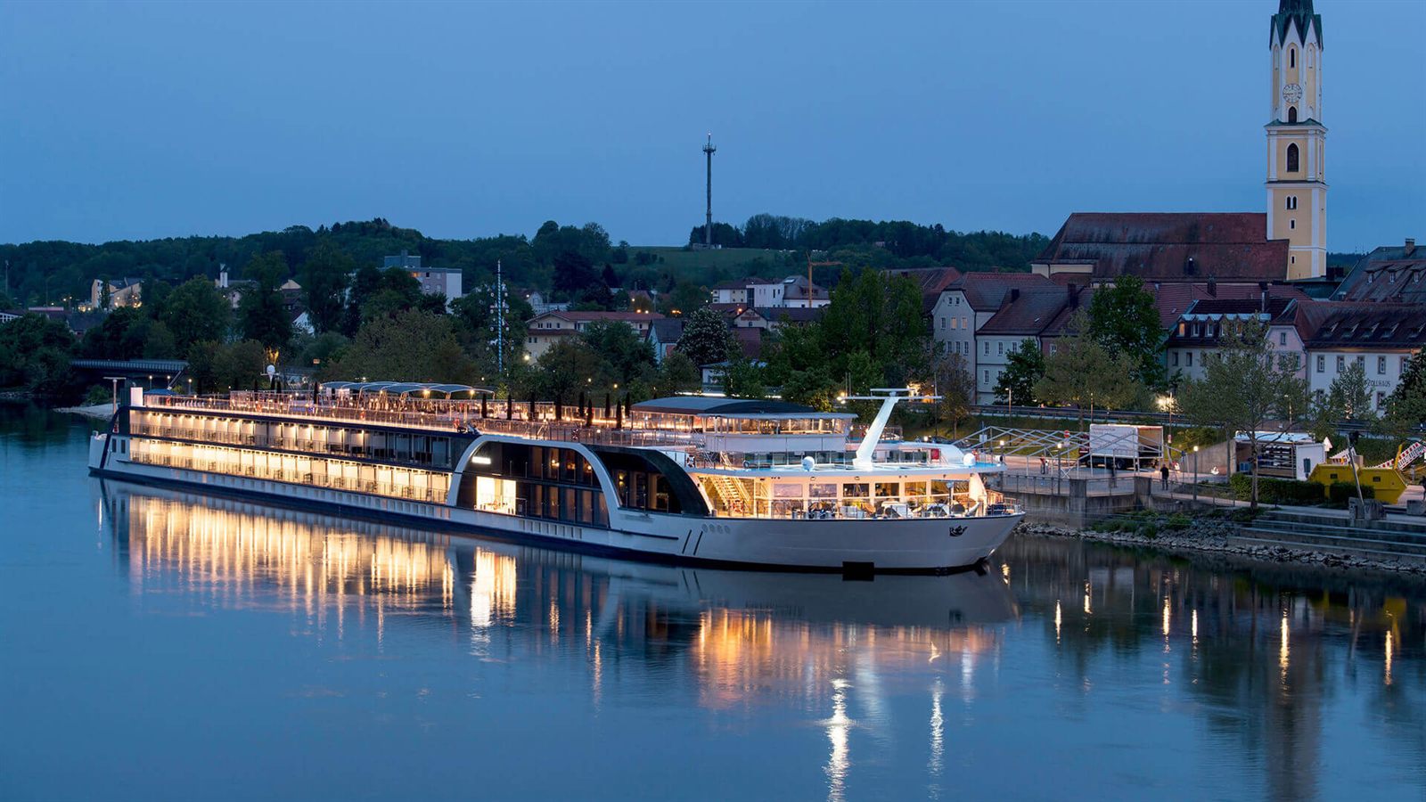 River cruise ship lit up at dusk along a European town waterfront